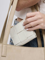 Person holding a White woven wallet with a beige handbag in the background