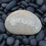 Stone with 'God Rocks' engraved on it surrounded by black pebbles