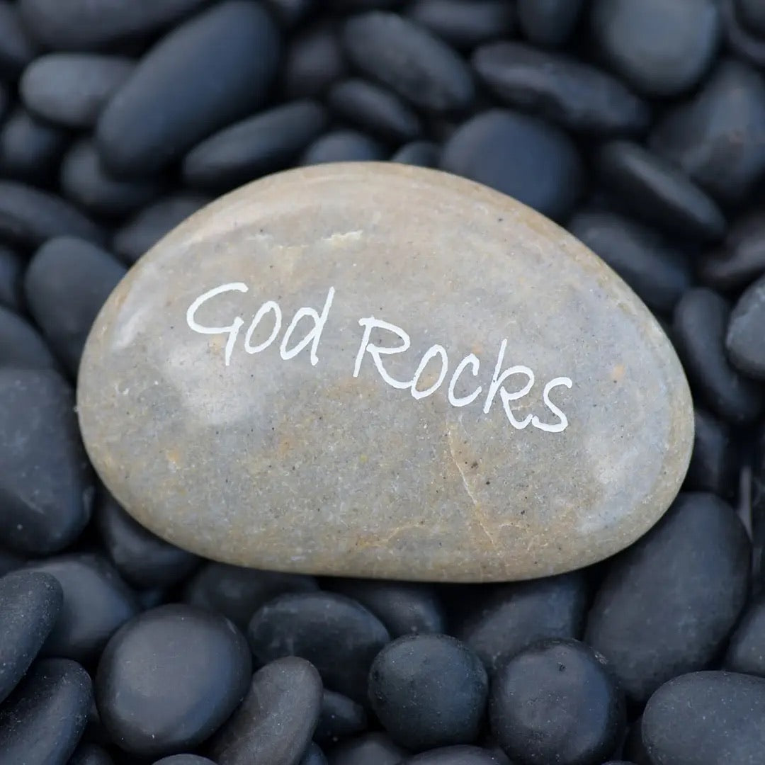 Stone with 'God Rocks' engraved on it surrounded by black pebbles