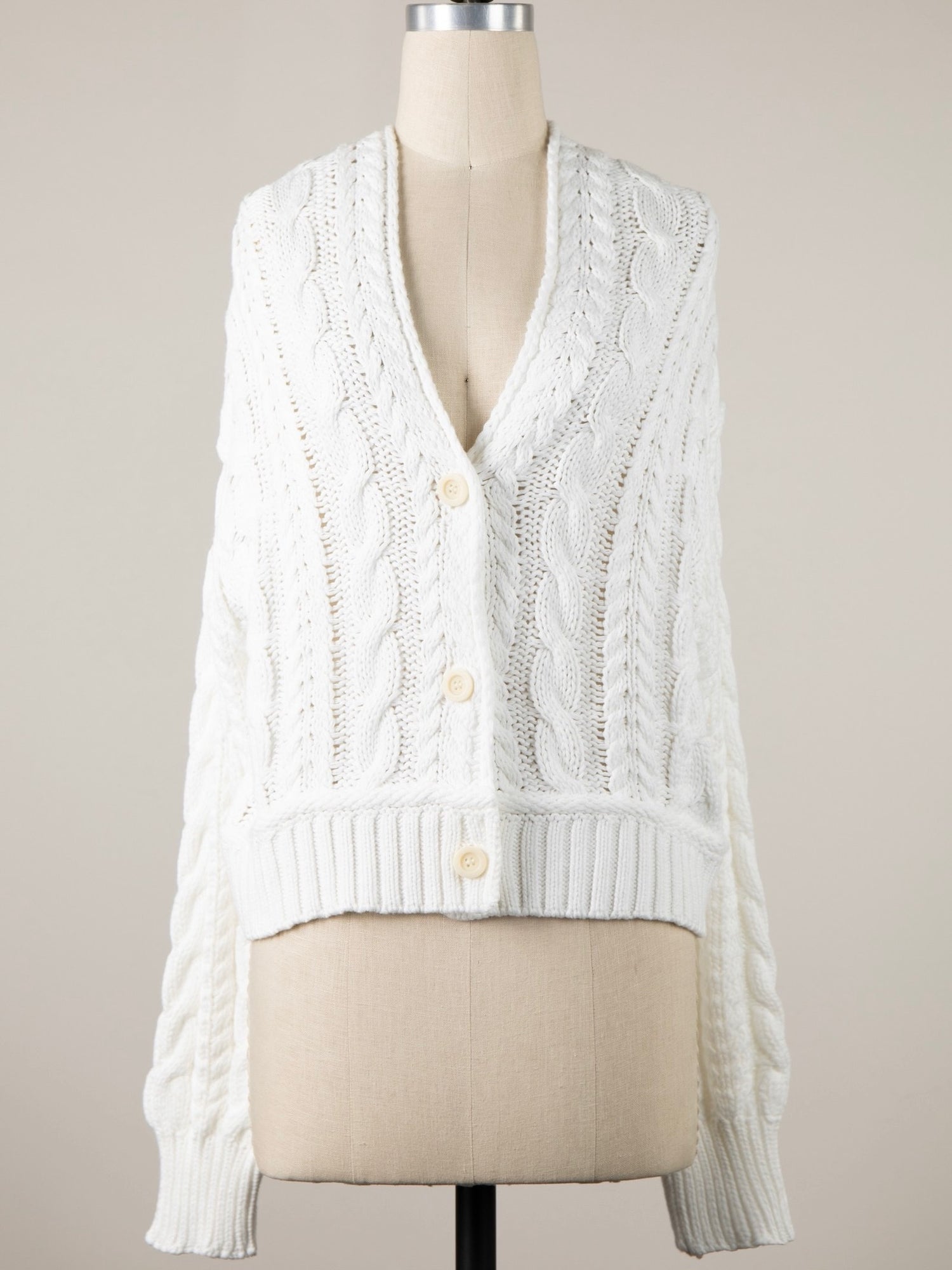 White cable knit cardigan on a mannequin against a neutral background