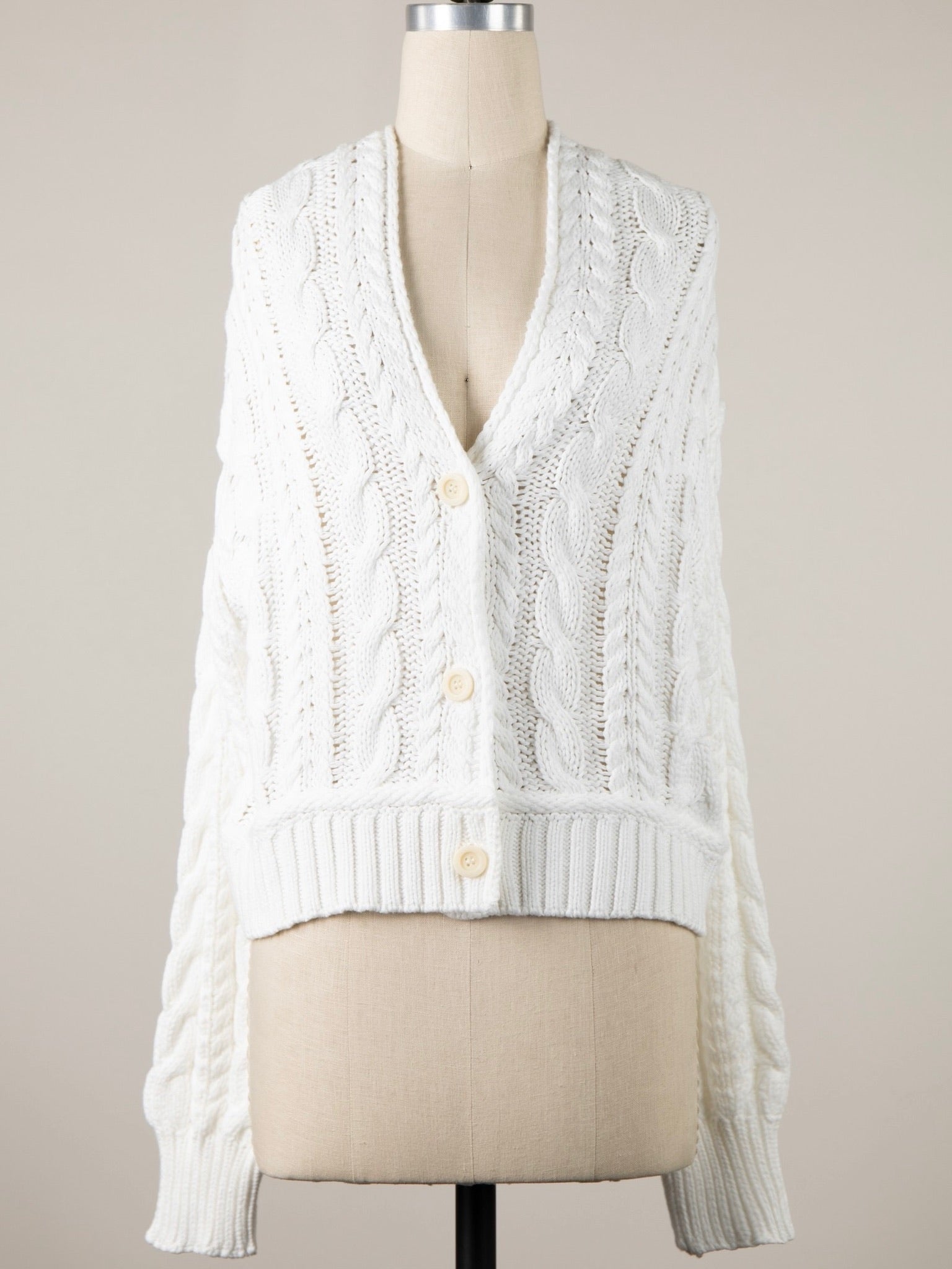 White cable knit cardigan on a mannequin against a neutral background