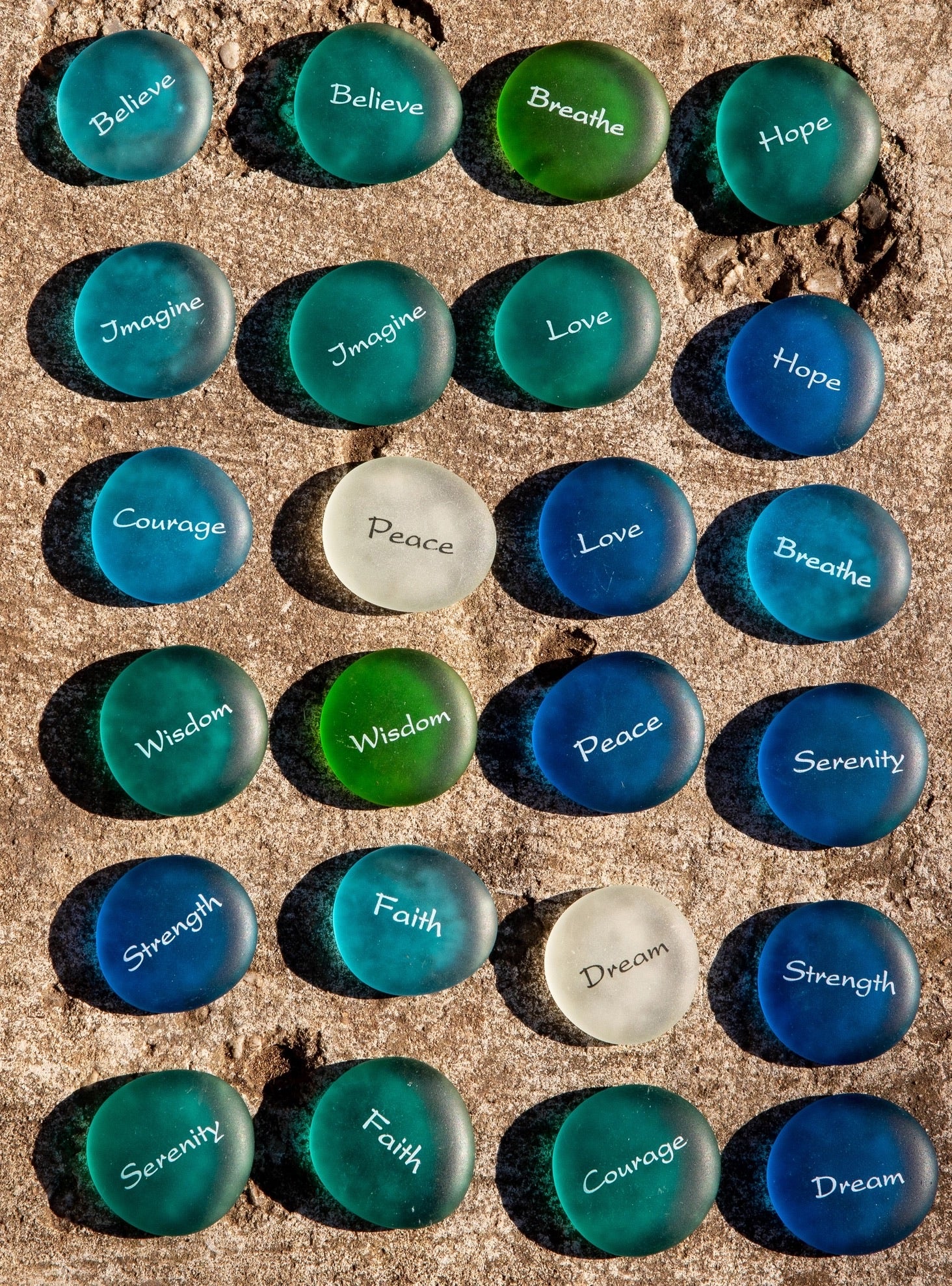 Set of sea glass pebbles with motivational phrases on a textured surface