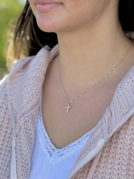 Close-up of a person wearing a delicate necklace with a cross pendant.
