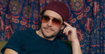 Person wearing Camp Eyewear Grateful Dead Forever sunglasses with a translucent champagne frame, walnut wood temples, and brown gradient polarized lenses.