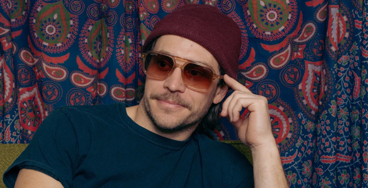 Person wearing Camp Eyewear Grateful Dead Forever sunglasses with a translucent champagne frame, walnut wood temples, and brown gradient polarized lenses.