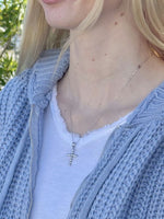 Person wearing a light blue cardigan and white shirt with a cross necklace.