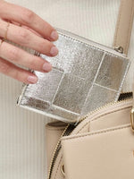 Silver quilted wallet held by a hand against a beige background