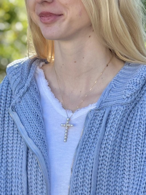 Person wearing a light blue knitted sweater with a cross necklace.