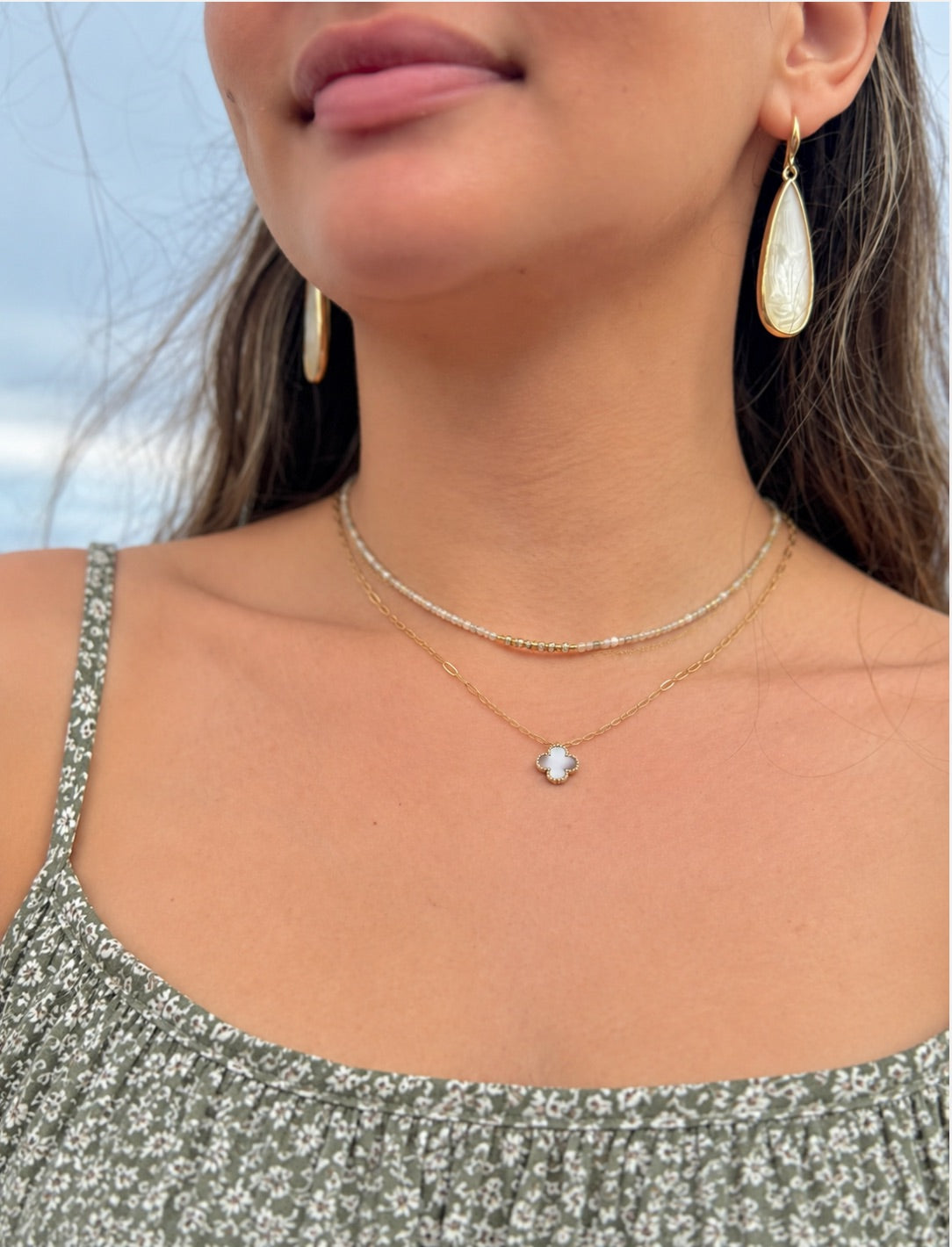 Gold teardrop earrings with pearlescent white inlay worn with layered gold and beaded necklaces at Ardor Boutique.