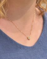 Gold necklace with a small round pendant worn by a person in a blue sweater.