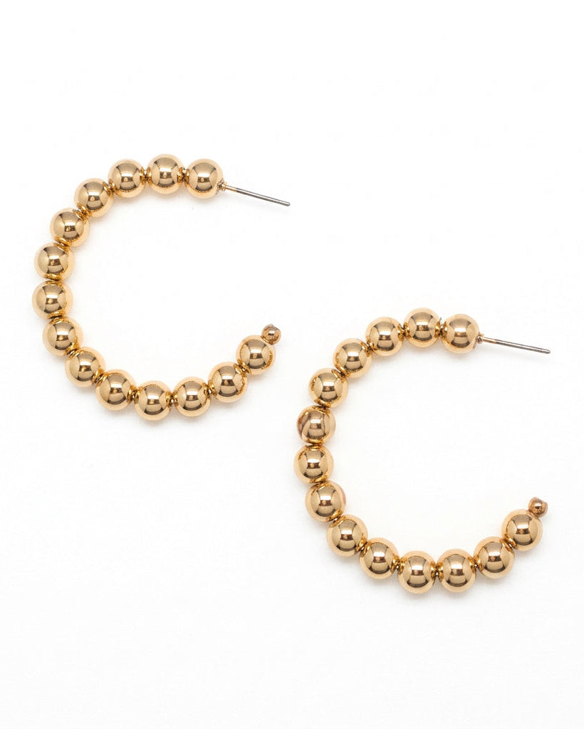 Flat lay of gold beaded hoop earrings on a white background, showing circular design with polished bead detail.