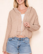 Model wearing the Kennedy Hoodie in sandy beige with a cropped relaxed fit, silver ring-pull zipper, drawstring hood, and distressed knit hem and sleeves.