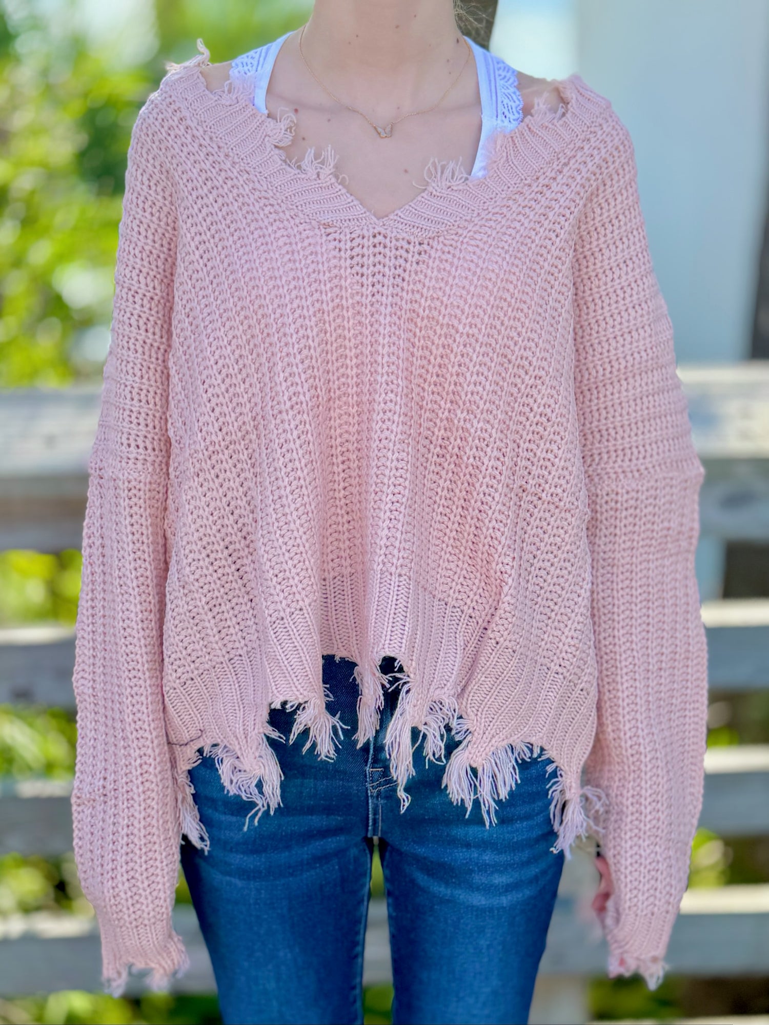 Pink distressed sweater worn by a person with a blurred background
