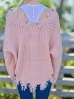 Person wearing a pink distressed sweater with a blurred outdoor background