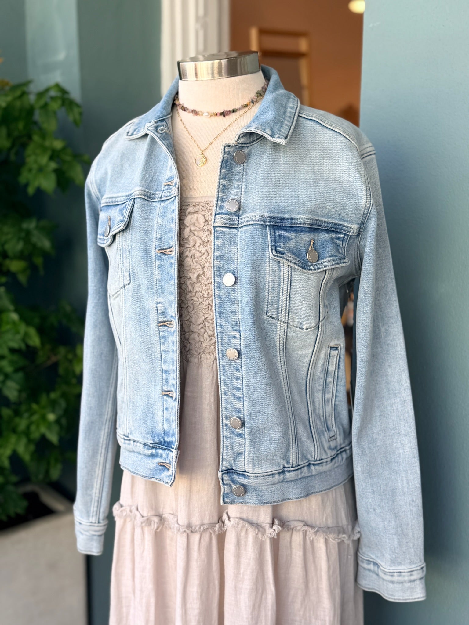 Light wash denim jacket layered over cream sleeveless tiered midi dress on mannequin