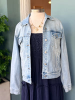 Light wash denim jacket layered over navy sleeveless tiered dress on mannequin