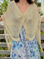 Woman wearing gold knit wrap sweater front view with a blue and gold dress and a blue necklace outdoors