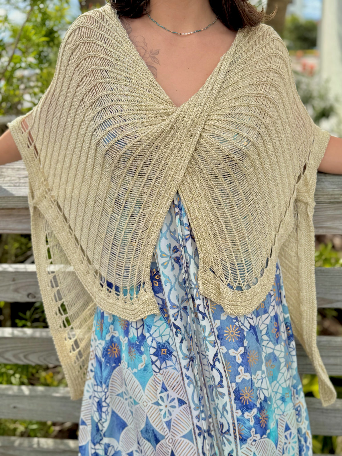Woman wearing gold knit wrap sweater front view with a blue and gold dress and a blue necklace outdoors