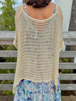 Woman wearing gold knit wrap sweater back view with a blue and gold dress and a blue necklace outdoors