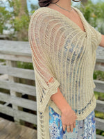 Woman wearing gold knit wrap sweater side view with a blue and gold dress and a blue necklace outdoors