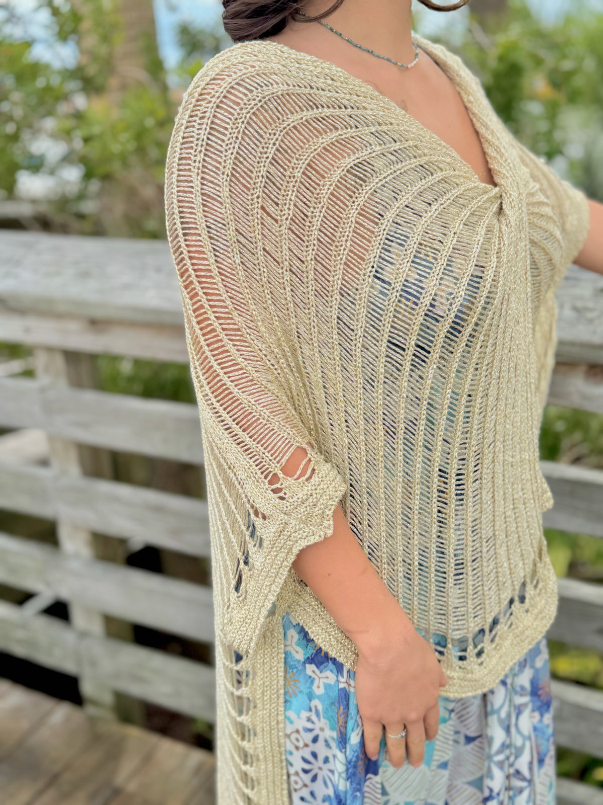 Woman wearing gold knit wrap sweater side view with a blue and gold dress and a blue necklace outdoors