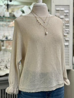 Champagne cream knit sweater with a loose, airy fit and gathered cuffs, styled with layered pearl necklaces and denim.