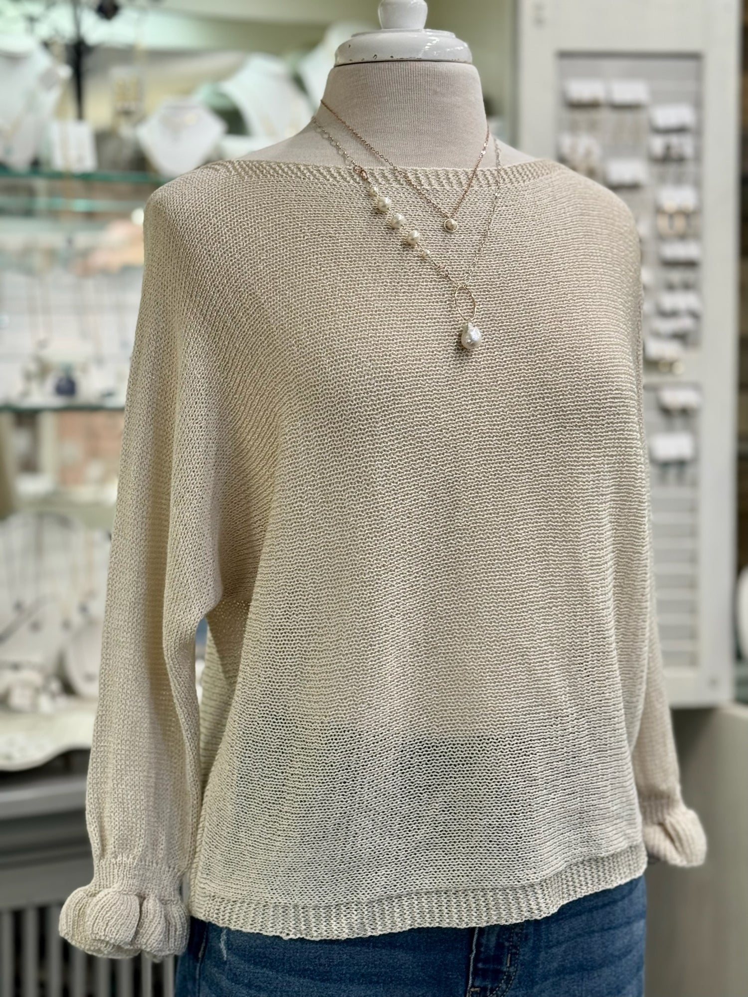 Champagne cream knit sweater with a loose, airy fit and gathered cuffs, styled with layered pearl necklaces and denim.