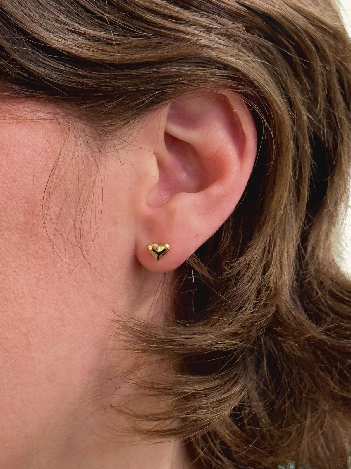 A pair of small gold heart stud earrings being worn