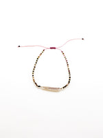 A purple bracelet with a baroque-style pearl and earthy-toned beads, featuring a sliding knot closure.