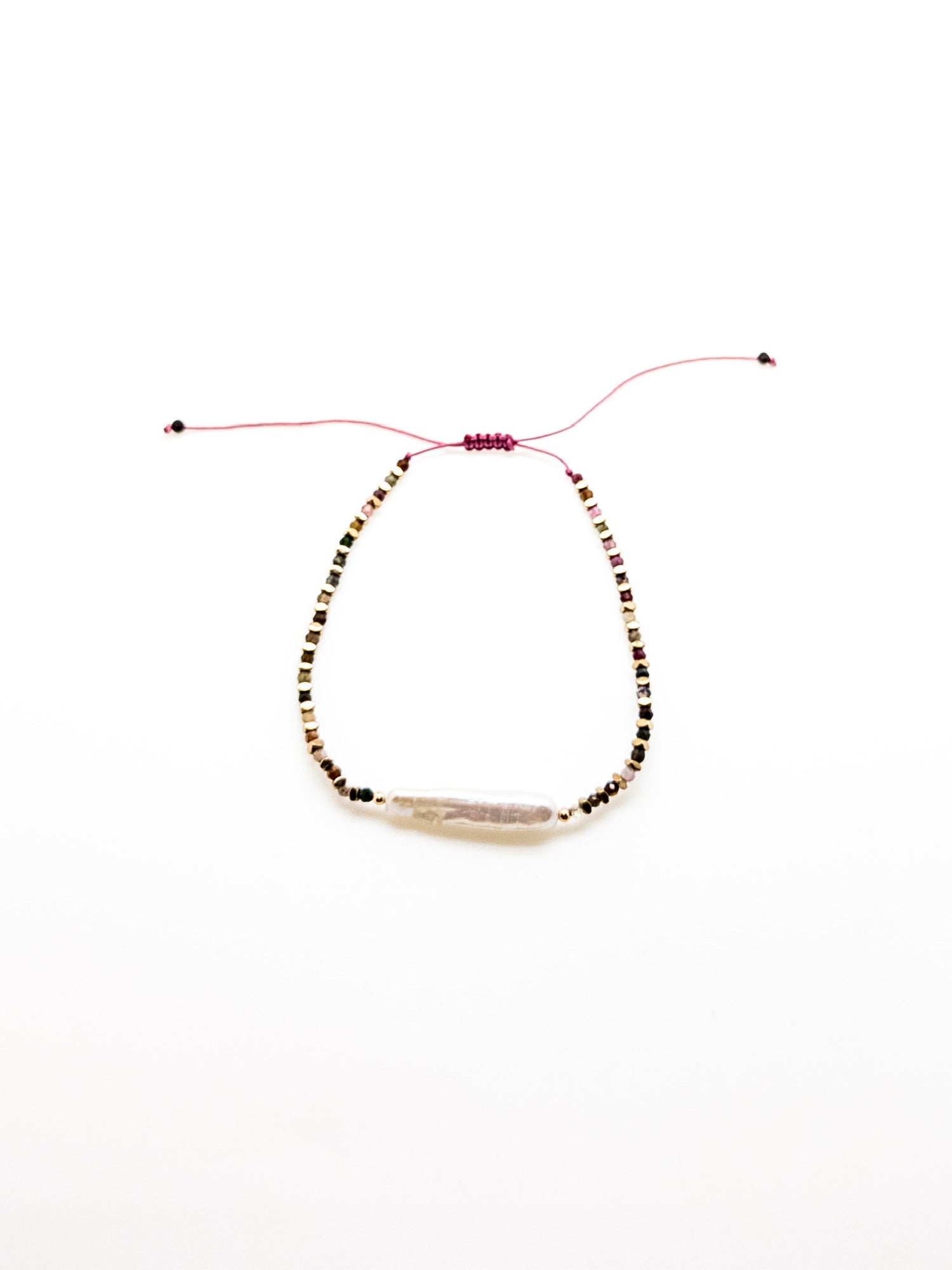 A purple bracelet with a baroque-style pearl and earthy-toned beads, featuring a sliding knot closure.