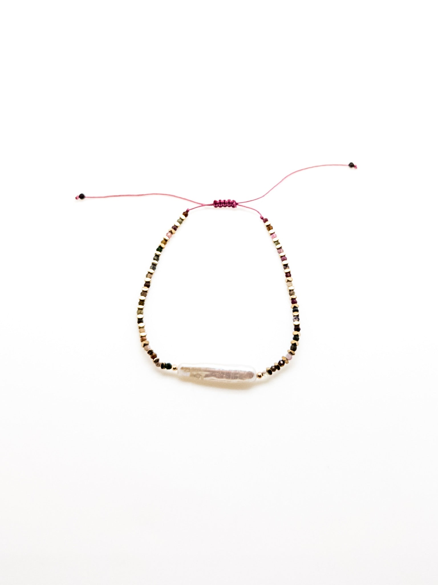 A purple bracelet with a baroque-style pearl and earthy-toned beads, featuring a sliding knot closure.
