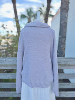 Soft grey fuzzy knit sweater with a cowl neck on a mannequin outdoors with a white skirt back view 