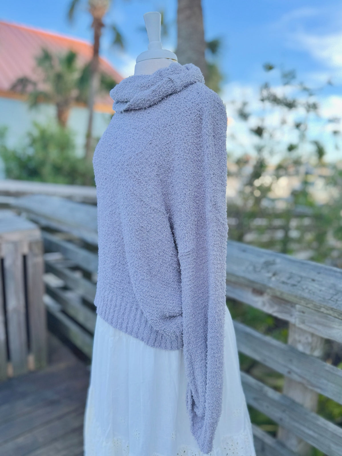 Soft grey fuzzy knit sweater with a cowl neck on a mannequin outdoors with a white skirt side view 
