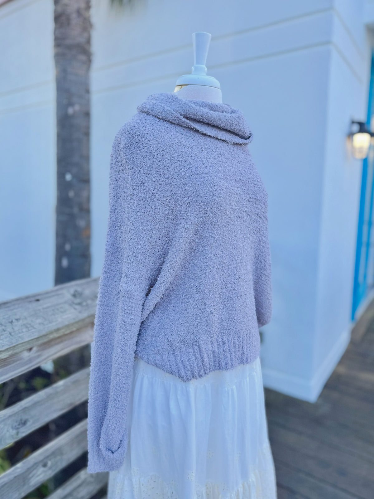 Soft grey fuzzy knit sweater with a cowl neck on a mannequin outdoors with a white skirt side view 