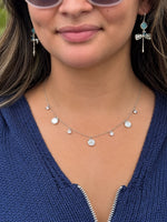 Close-up of the Melody Silver Necklace featuring a delicate silver-tone chain with round white mother-of-pearl inspired charms and small sparkling accents, modeled with a navy knit sweater.