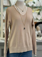 Blush taupe knit V-neck sweater on a mannequin, featuring a relaxed fit with ribbed hem and side slits, layered with gold necklaces.