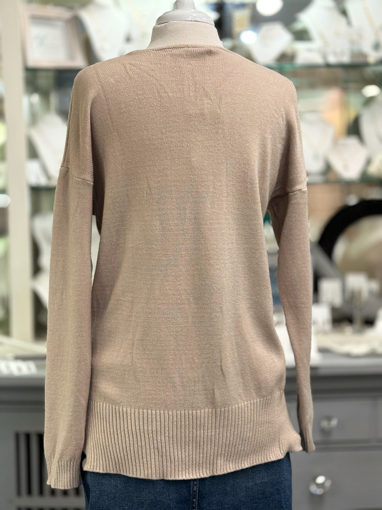 Back view of a soft blush taupe sweater with a relaxed silhouette, drop shoulder sleeves, and wide ribbed hemline.
