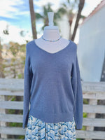 Dark grey knit sweater with blue beaded necklace and a blue colorful dress underneath 