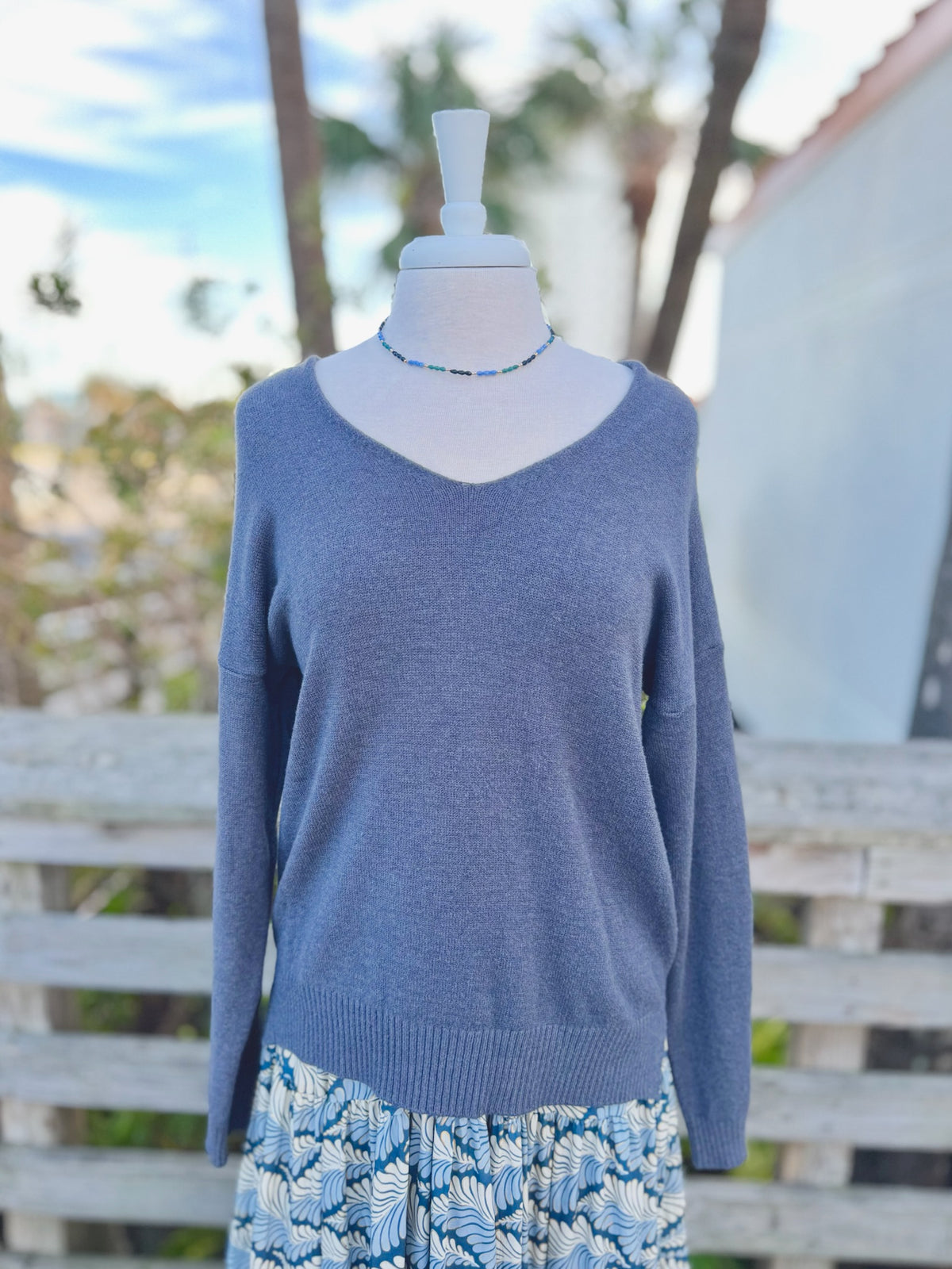 Dark grey knit sweater with blue beaded necklace and a blue colorful dress underneath 