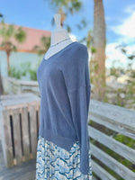Side view of a dark grey knit sweater with blue beaded necklace and a blue colorful dress underneath 