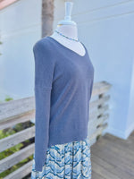 Side view of a dark grey knit sweater with blue beaded necklace and a blue colorful dress underneath 