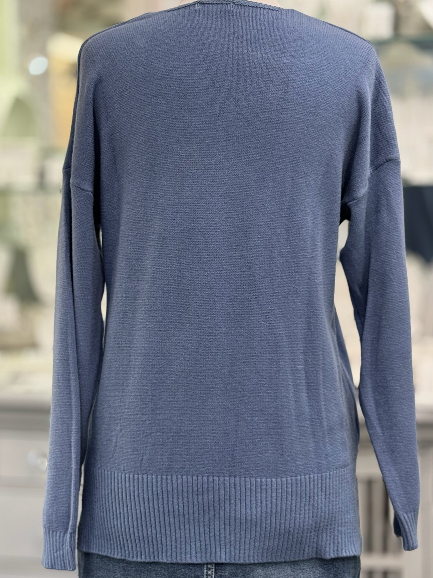 Back view of dusty blue knit sweater with relaxed fit, long sleeves, and thick ribbed hem detail.