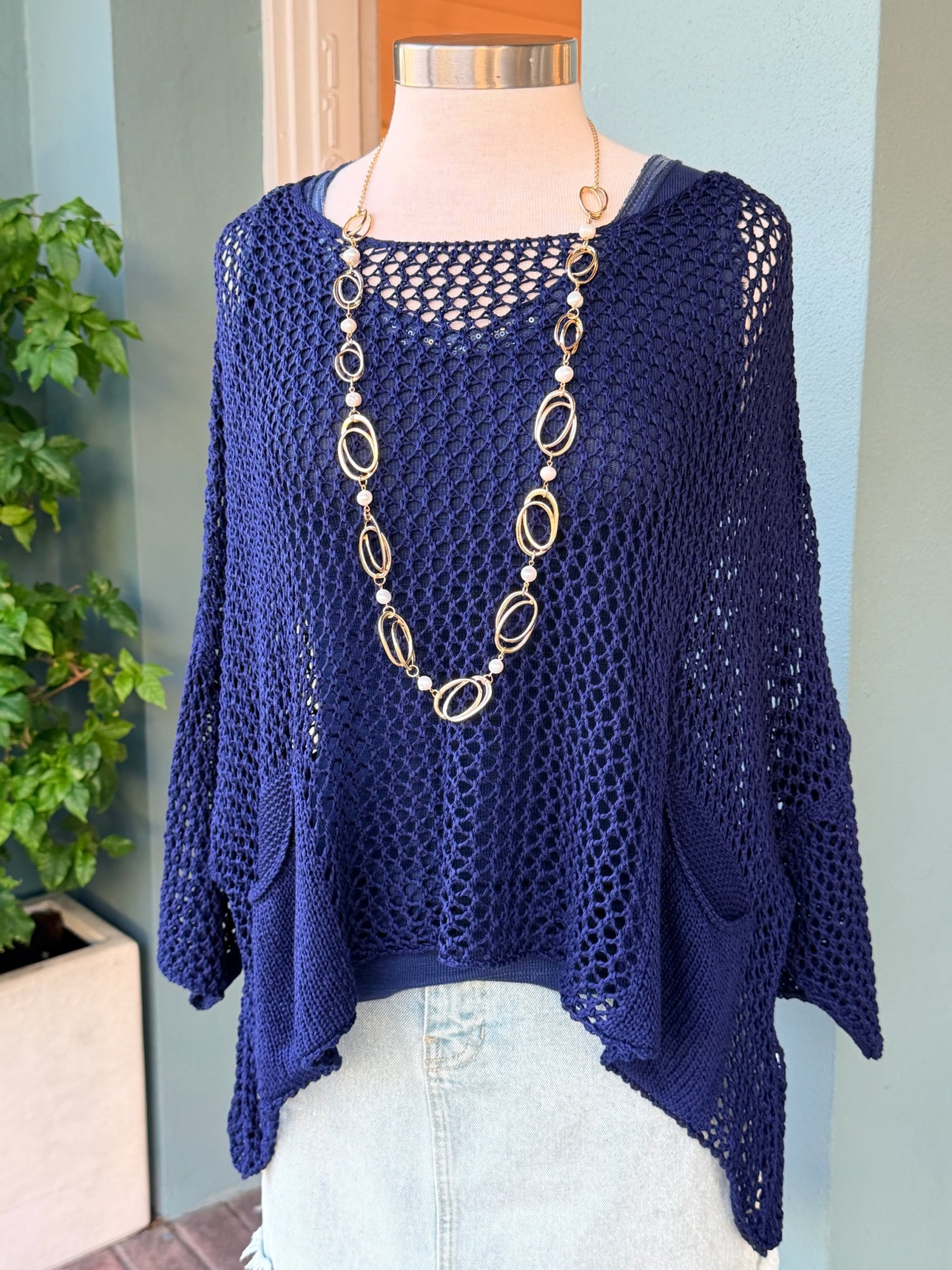 Navy blue crochet top on a mannequin with a long necklace against a light blue wall.
