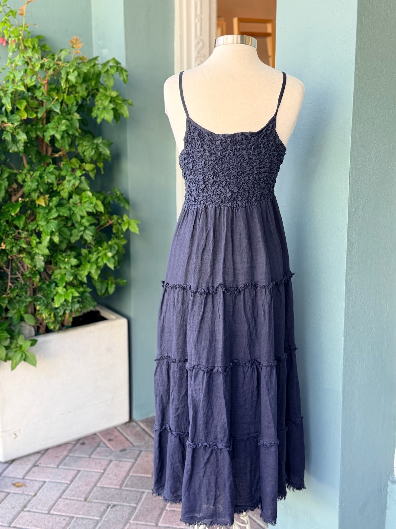 Navy tiered sleeveless dress with textured bodice and thin straps shown from back on mannequin