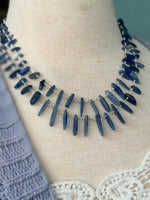 Close-up of a blue statement necklace and lace camisole layered under the Isabelle Sweater Cardigan in blue grey at Ardor Boutique.