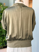 Olive green jacket on a mannequin against a light blue wall.