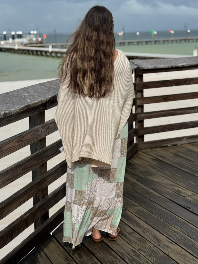 Back view of the Patty Patchwork Print Smocked Maxi Dress featuring a flowing patchwork skirt in soft pastel colors, layered with a cream knit wrap poncho at Ardor Boutique.