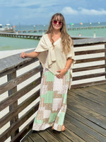 Patty Patchwork Print Smocked Maxi Dress in mint green, blush pink, and cream, styled with a cream knit wrap poncho on a waterfront boardwalk at Ardor Boutique.