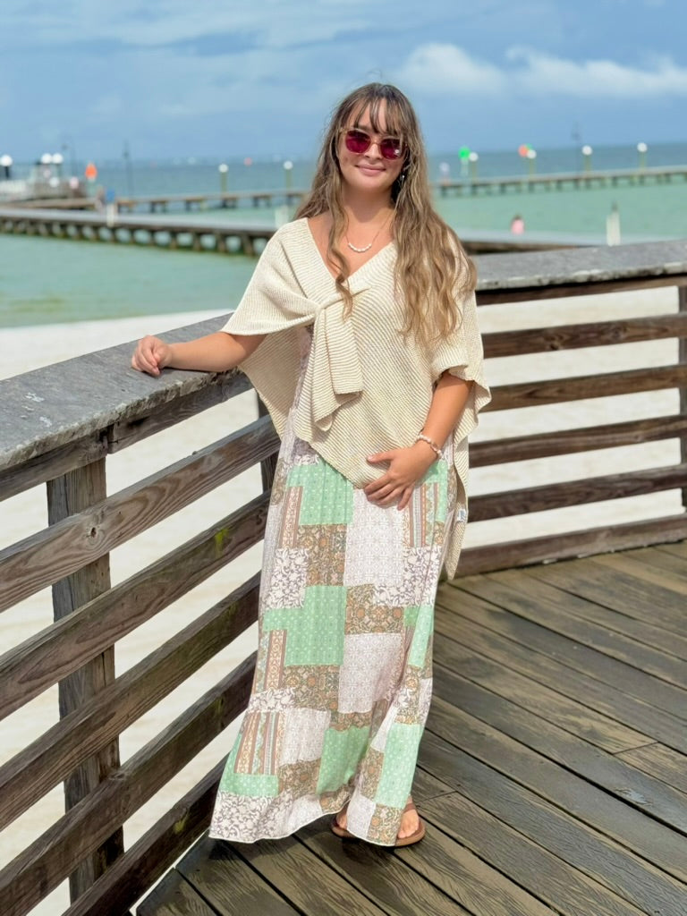 Patty Patchwork Print Smocked Maxi Dress in mint green, blush pink, and cream, styled with a cream knit wrap poncho on a waterfront boardwalk at Ardor Boutique.