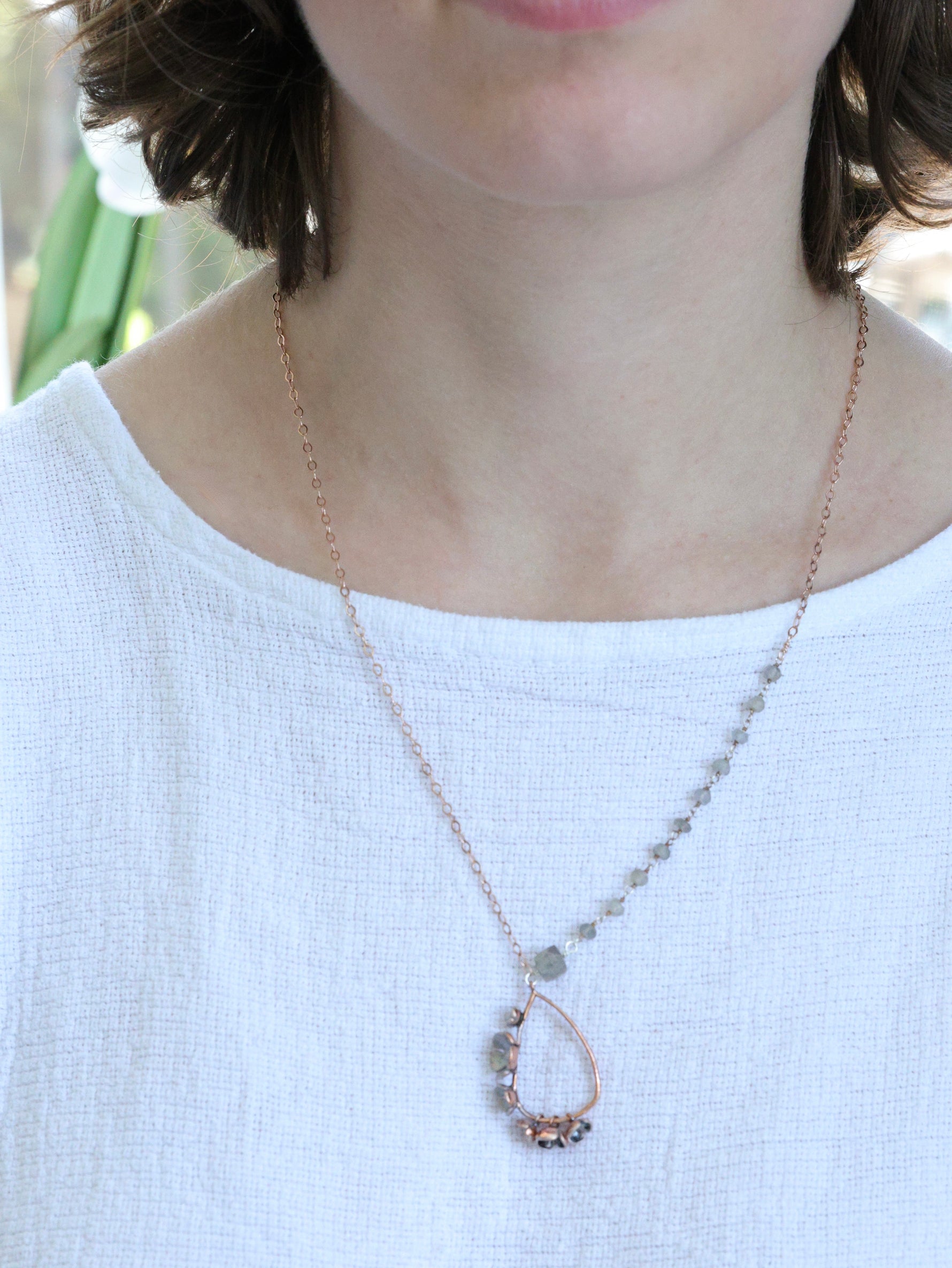 Woman wearing a Rose gold teardrop necklace with labradorite gemstones and asymmetrical chain, handcrafted by Nina Halls for Ardor Boutique.